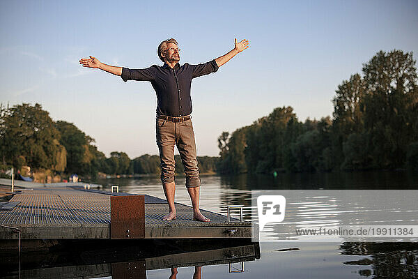 Senior man standing with arms outstretched on jetty