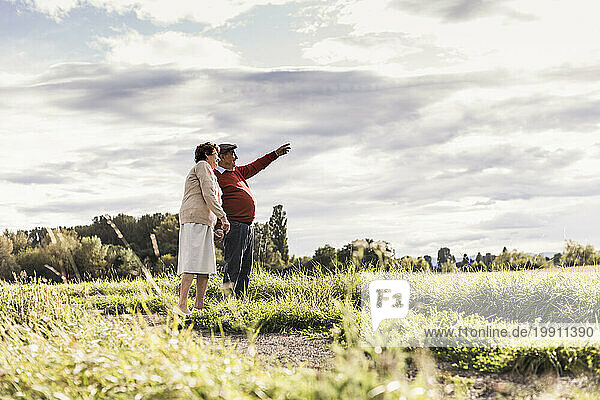 Senior man gesturing with woman standing at field on sunny day