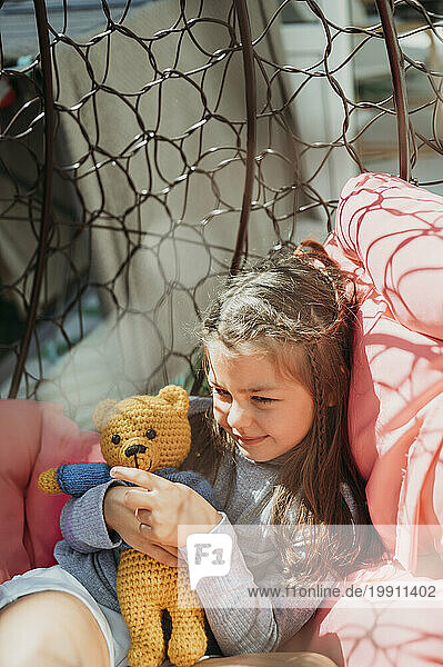 Smiling girl playing with stuffed toy in porch swing