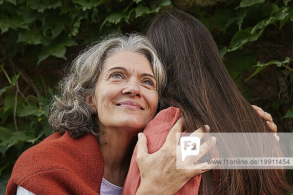 Smiling mother hugging daughter near plants