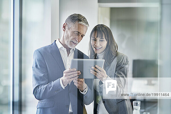 Smiling business people having discussion over tablet PC in office