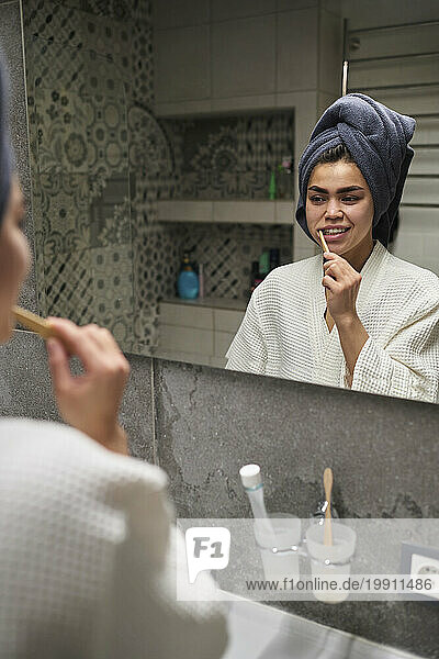 Young woman brushing teeth and looking in mirror at home