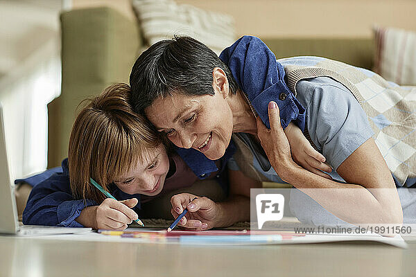 Girl with Down syndrome embracing mother and drawing together on paper at home