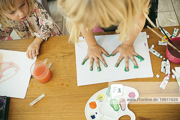 Girl making handprint with watercolors on paper at home