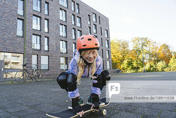 Happy girl crouching and skateboarding on street