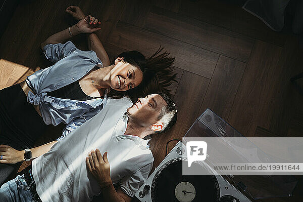 Smiling couple lying on floor near turntable at home