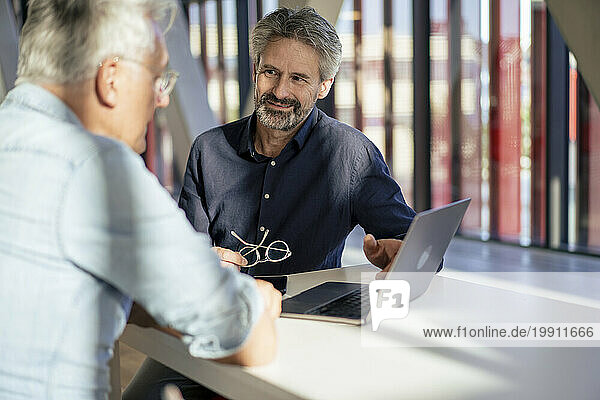 Smiling senior businessman discussing with colleague over laptop at table