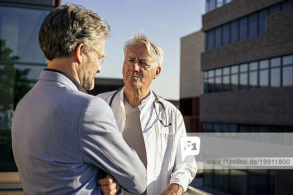Smiling senior doctor discussing with patient on balcony at sunny day