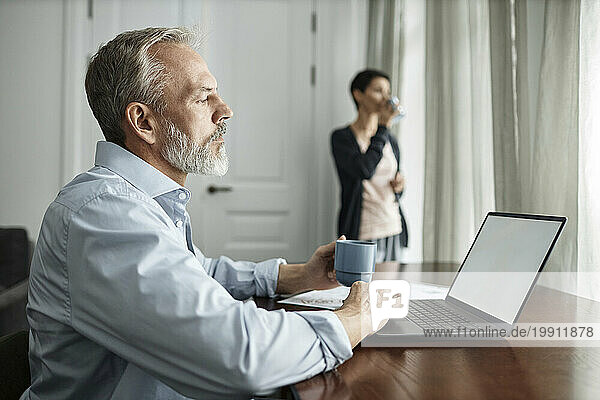 Man using laptop and drinking tea while spending time at home with wife
