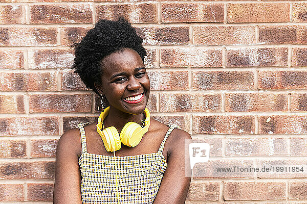 Smiling woman with headphones around neck in front of brick wall