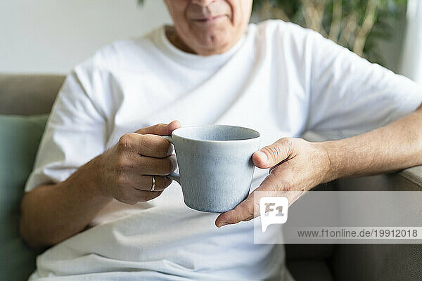 Senior man holding coffee cup in living room at home