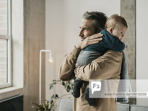 Father carrying baby boy in front of wall at home