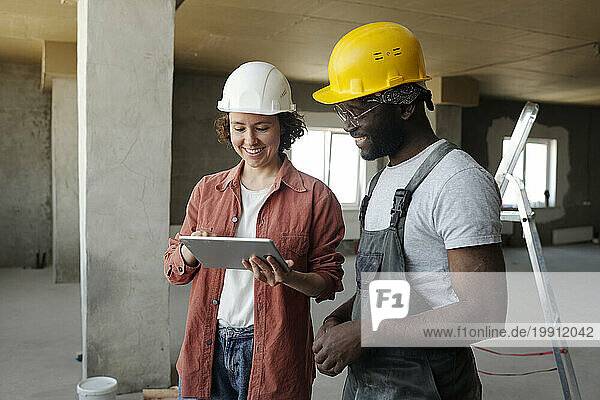 Smiling engineer discussing with colleague over tablet PC at construction site