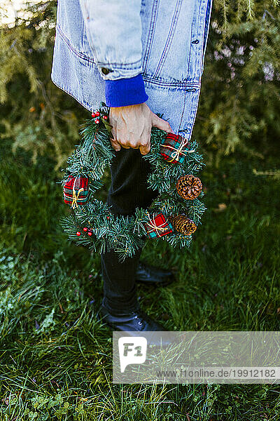 Man holding Christmas wreath and standing on grass