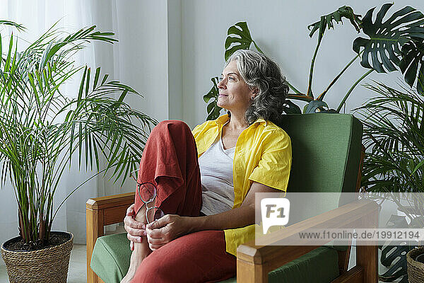 Thoughtful woman day dreaming sitting on armchair at home
