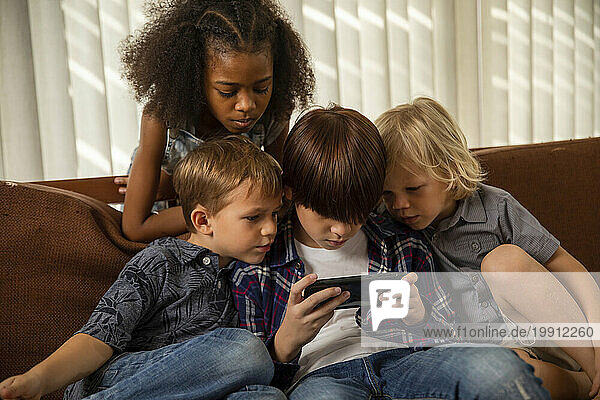 Boy playing game on smart phone with friends sitting on couch