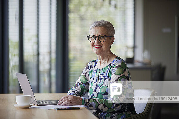 Smiling senior woman using laptop at table at home