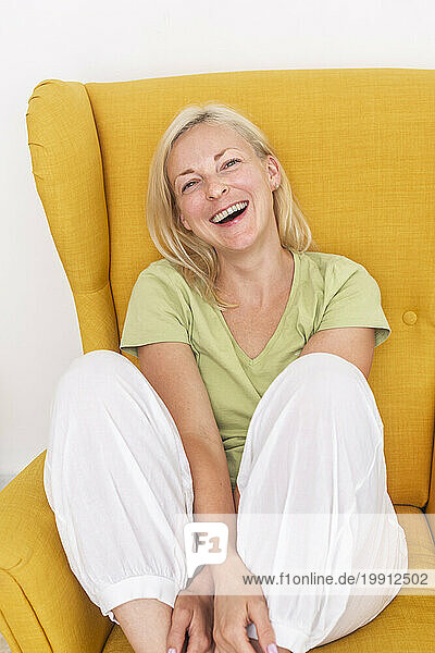 Happy woman laughing on armchair at home