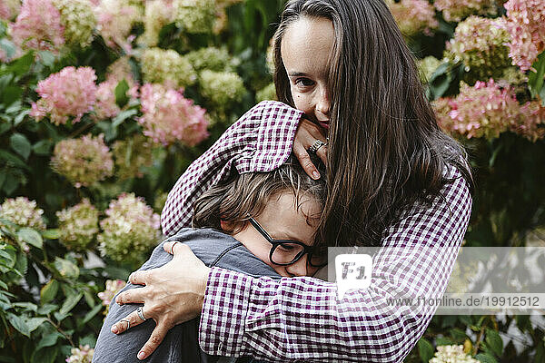 Mother embracing son near hydrangea flowers