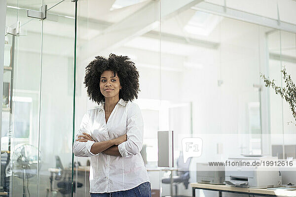 Businesswoman with arms crossed leaning on glass wall at office
