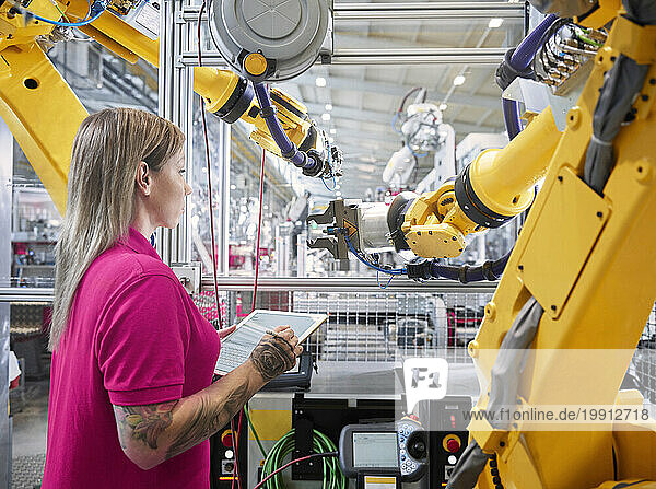 Technician examining robotic arms and holding tablet PC in industry