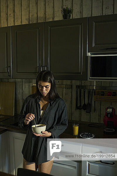 Woman holding bowl and having breakfast in kitchen at home