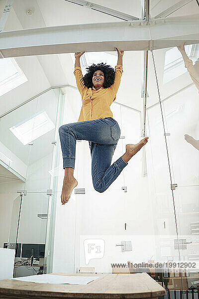 Playful businesswoman hanging on iron bar at office