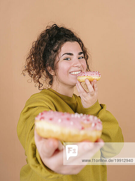 Smiling young woman showing and holding doughnuts against peach background