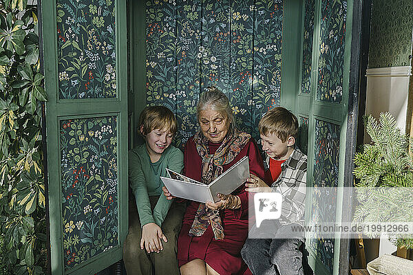 Great grandmother reading book to grandsons sitting in closet at home
