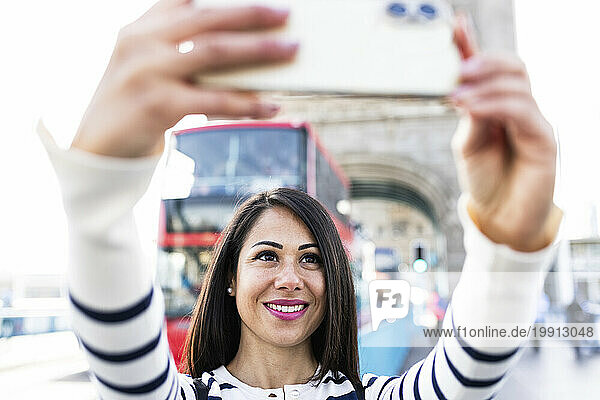 Happy woman taking selfie through smart phone in London city