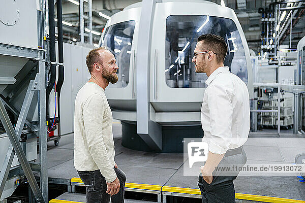 Employee and businessman talking at modern machine in a factory