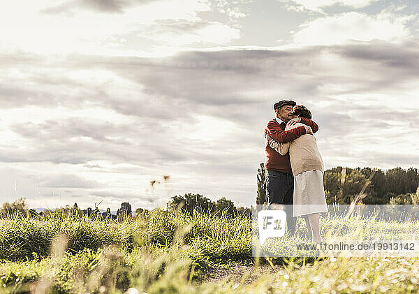 Loving senior couple hugging in field on sunny day