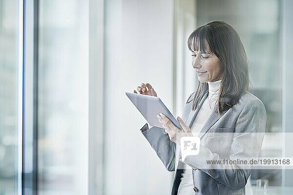 Smiling businesswoman using tablet PC seen through glass