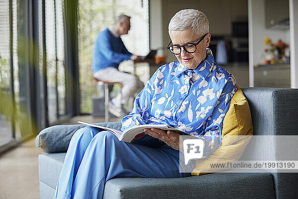 Senior woman sitting on couch at home reading magazine