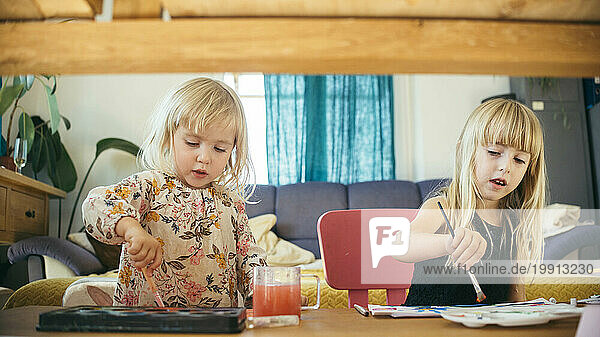 Girls painting with paintbrushes and watercolors at table in home