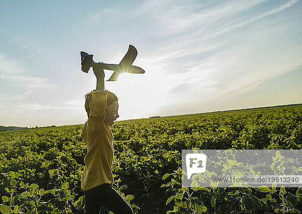 Cheerful boy running with toy airplane in agricultural field under sky