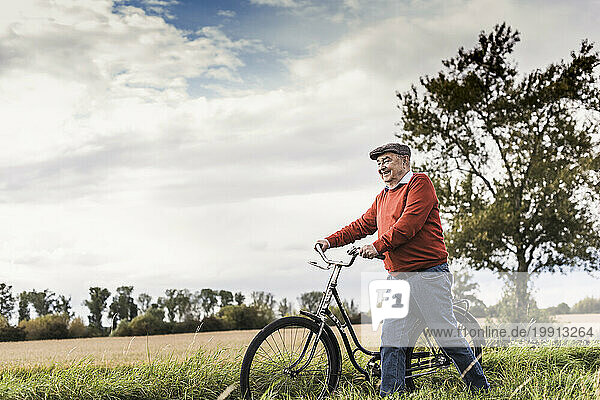 Smiling senior man walking with bicycle in field