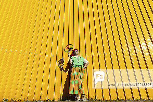 Happy senior woman holding pinwheel toy in front of yellow wall