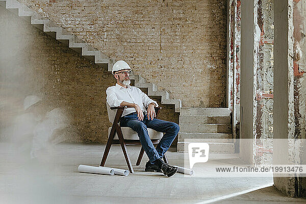 Contemplative architect wearing hardhat and sitting at construction site