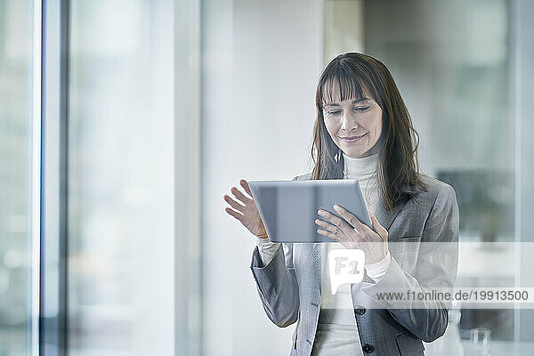 Smiling mature businesswoman using tablet PC seen through glass