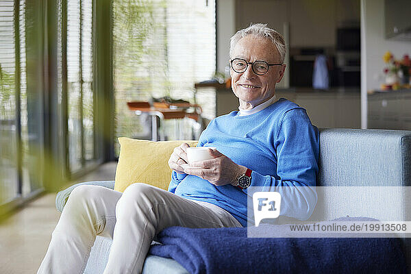Senior man sitting on couch at home with cup of coffee