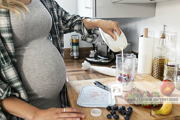 Pregnant woman pouring milk in measuring cup and preparing milkshake