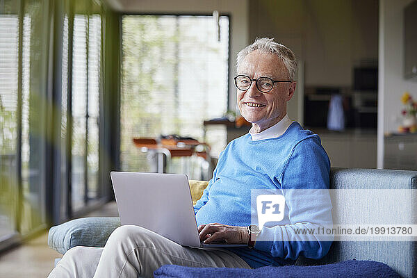 Smiling senior man using laptop on couch at home