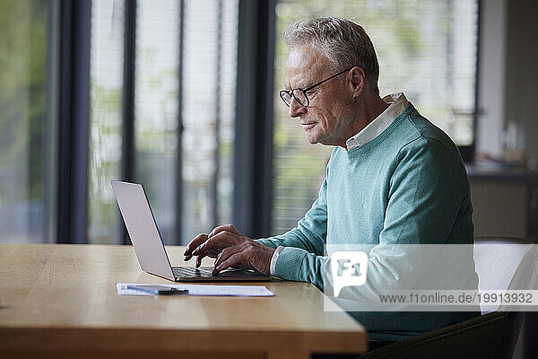 Senior man using laptop at table at home