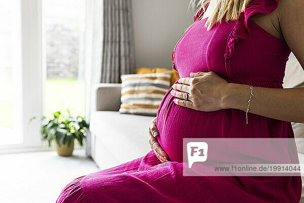 Pregnant woman sitting with hands on stomach at home