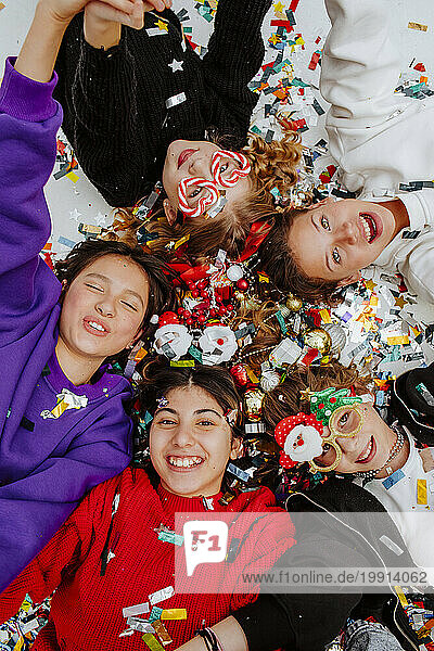 Happy friends lying near Christmas decorations on floor