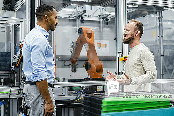 Employee and businessman talking at industrial robot in a factory