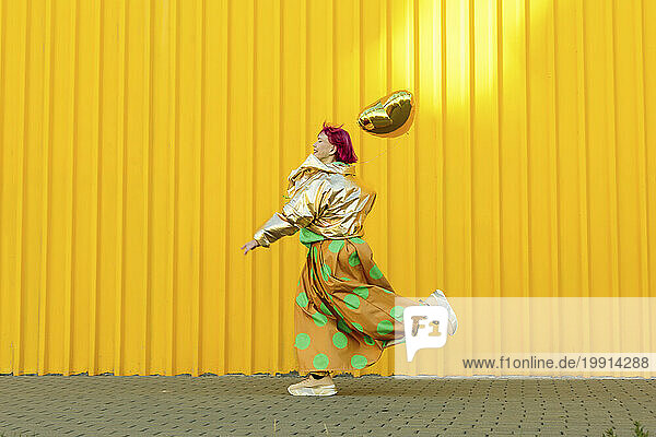 Senior woman running with heart shaped balloon in front of yellow wall
