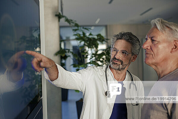 Senior doctor explaining man over device screen in hospital