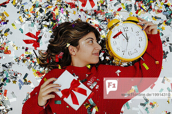 Happy girl lying near confetti with clock and gift boxes